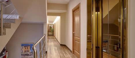A hallway with a wooden floor, a glass door, and a staircase with metal railings.