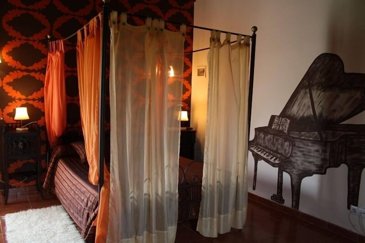 A bedroom with a bed, a piano, and curtains.