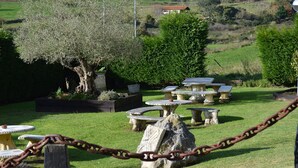 A garden with stone tables and chairs, surrounded by greenery and a large tree. - Posada El Valle (Suances)