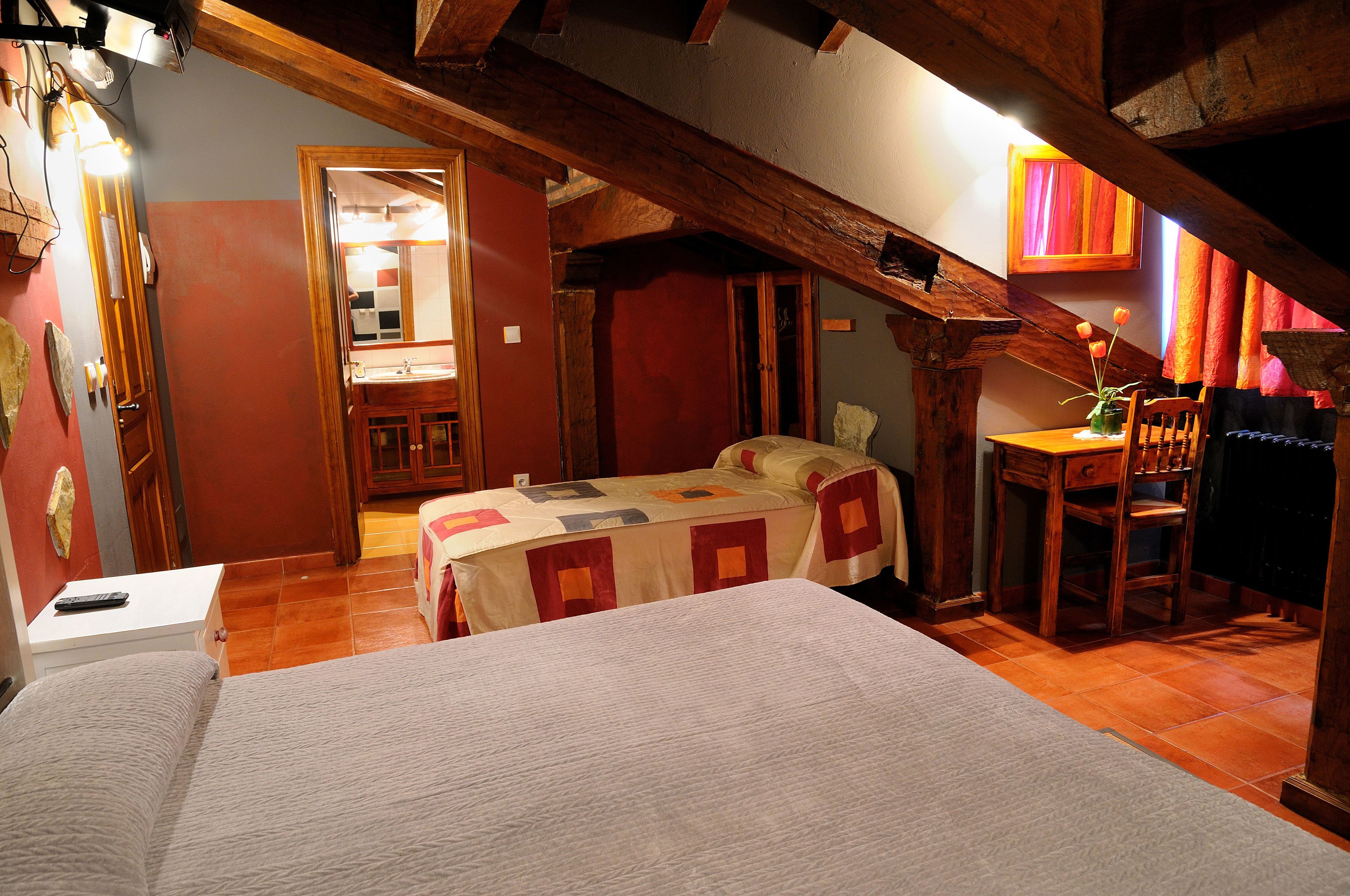 Un dormitorio con cama, escritorio y silla. Hay un espejo y una ventana con cortinas.