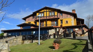 A two-story building with a yellow facade, stone foundation, and a balcony with a metal railing. - Posada El Valle (Suances)