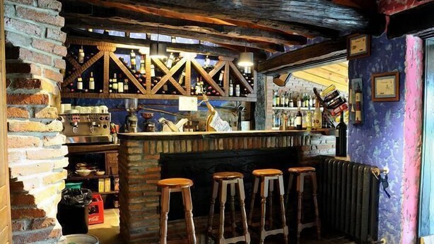 A rustic bar area with a brick wall, wooden stools, and a variety of bottles and glasses. - Posada El Valle (Suances)