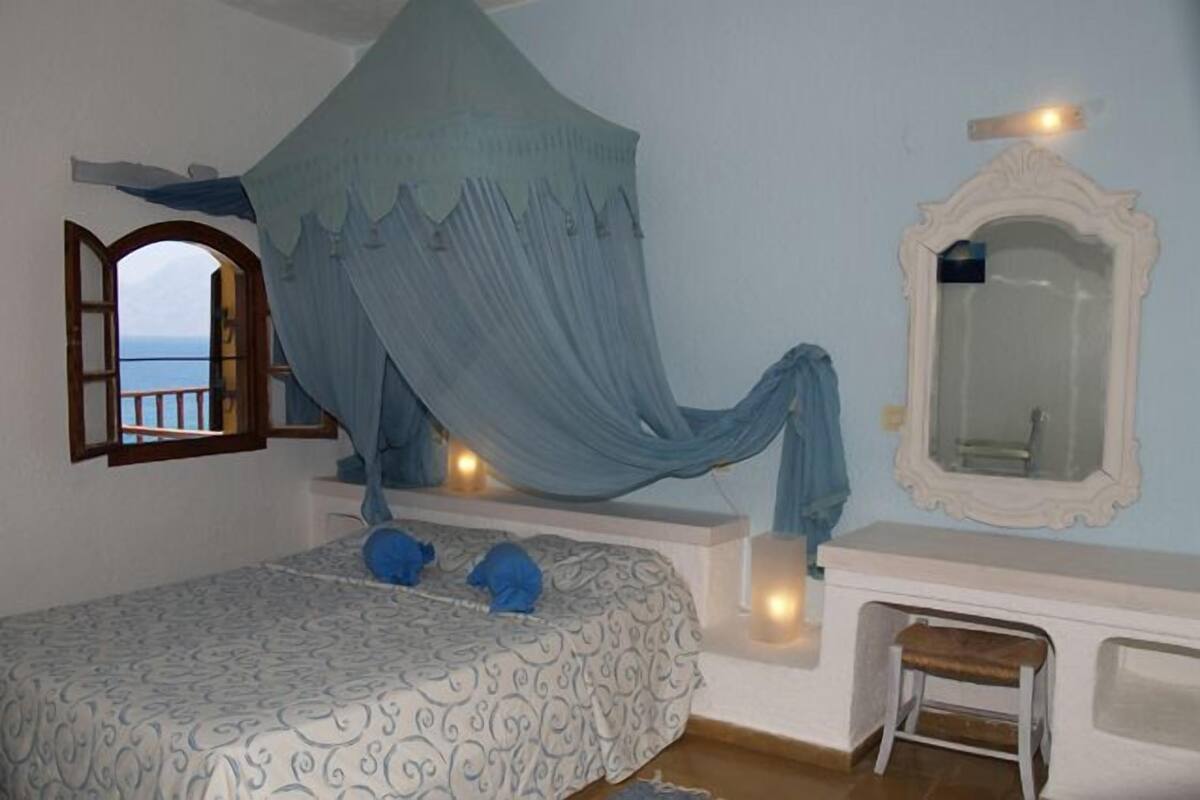 Ein Schlafzimmer mit Bett, Fenster mit Blick, Spiegel und einer Bank.