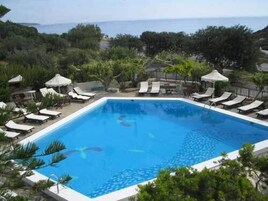 Una piscina al aire libre, sombrillas, sillones reclinables de piscina