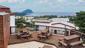 Terraza de madera con mesas de picnic que da a vistas costeras con edificios y follaje.