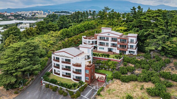 Un hotel de varios pisos con un diseño arquitectónico moderno, rodeado de exuberante vegetación y un telón de fondo montañoso.