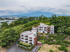 Un hotel de varios pisos con un diseño arquitectónico moderno, rodeado de exuberante vegetación y un telón de fondo montañoso.