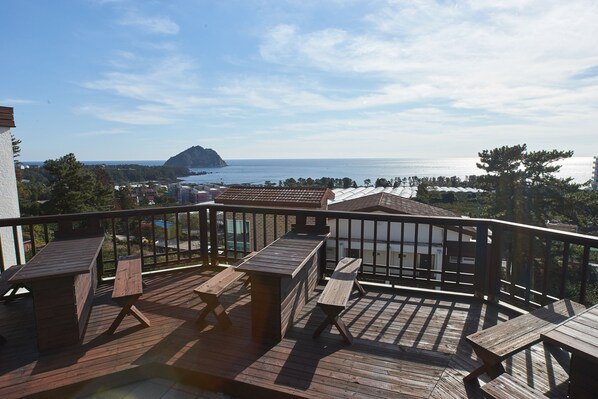 A wooden deck with picnic tables overlooking a coastal view. - Fourseason Pension (Seogwipo)