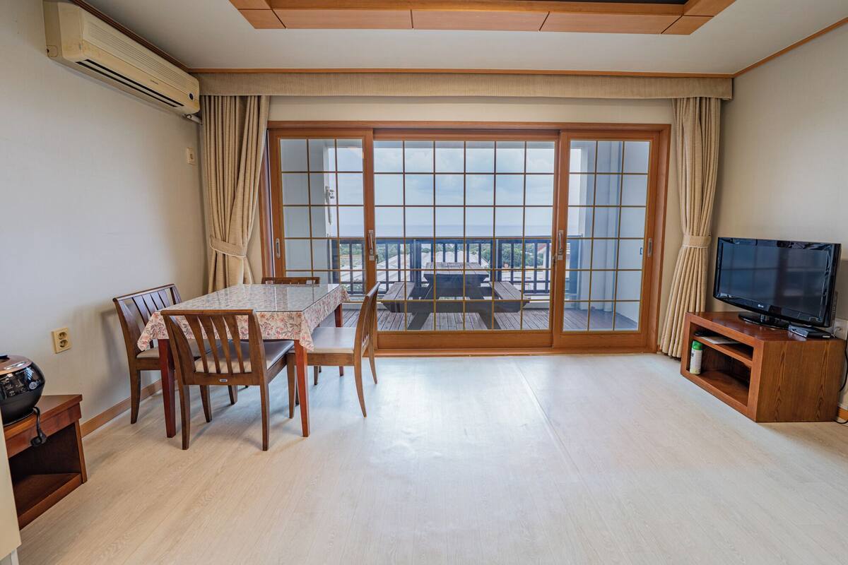 A living room with a dining table, chairs, a TV, and a balcony with a view.