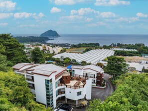 A coastal hotel with multiple buildings, including a prominent white structure with a balcony and a large greenhouse area. - Fourseason Pension (Seogwipo)