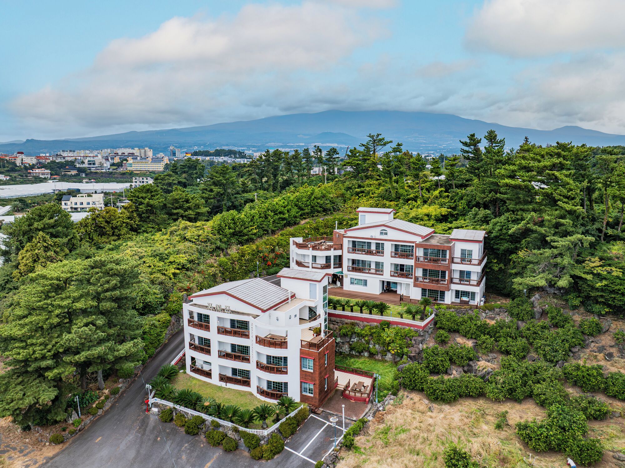 A multi-story hotel with a modern architectural design, surrounded by lush greenery and a mountainous backdrop.