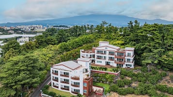 A multi-story hotel with a modern architectural design, surrounded by lush greenery and a mountainous backdrop.