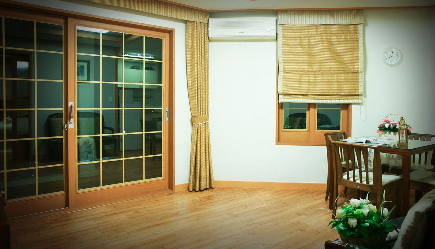 A room with a sliding glass door, a window with a blind, a wooden table with chairs, and a small potted plant.
