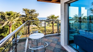 A balcony with a glass railing, a round table with chairs, and a sofa. - Beewool Chaewool (Seogwipo)