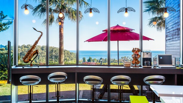 A bar area with a view of the ocean, a saxophone, and a red umbrella. - Beewool Chaewool (Seogwipo)