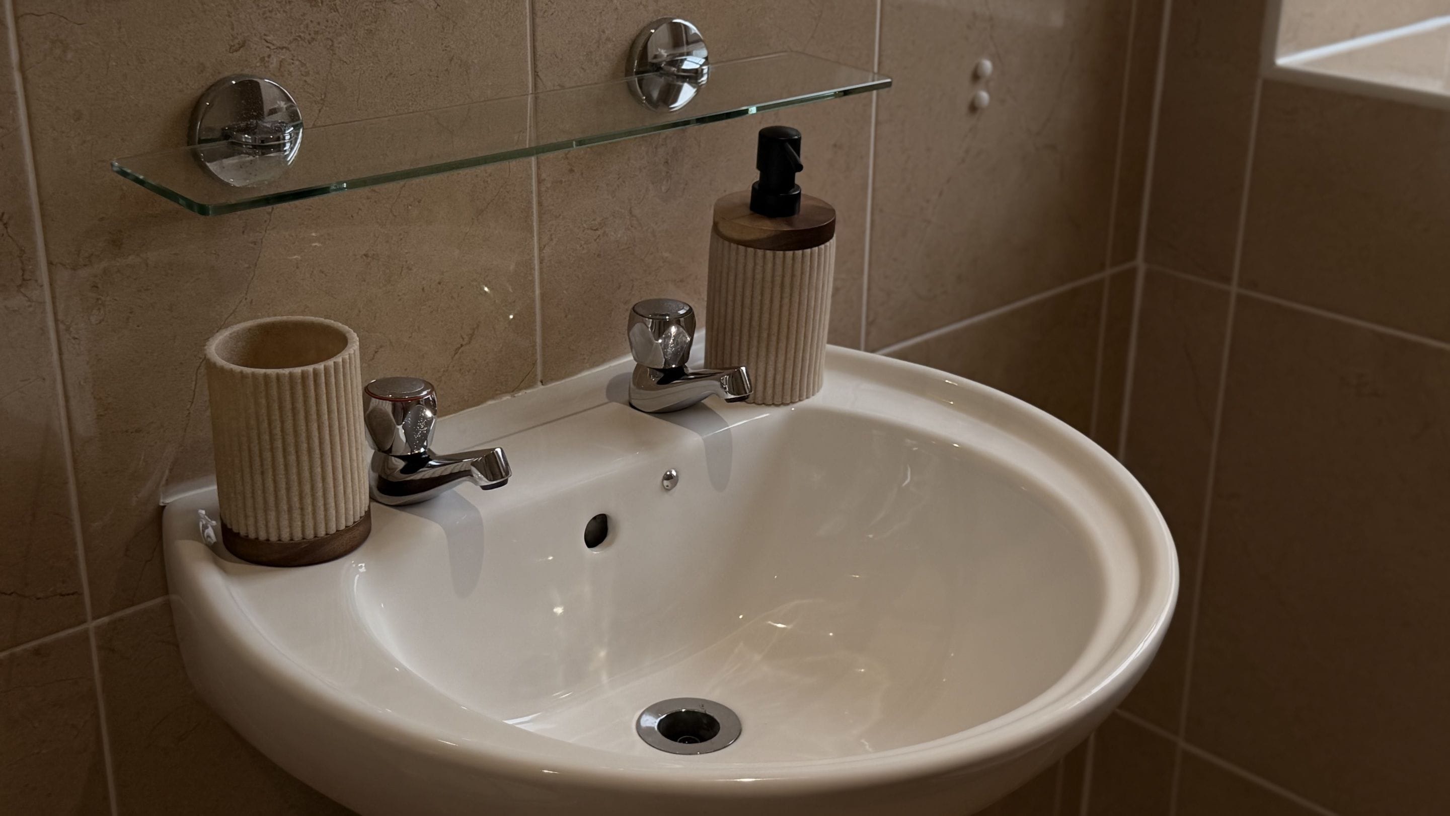 A bathroom sink with a glass shelf above it, a towel holder, and a cup.