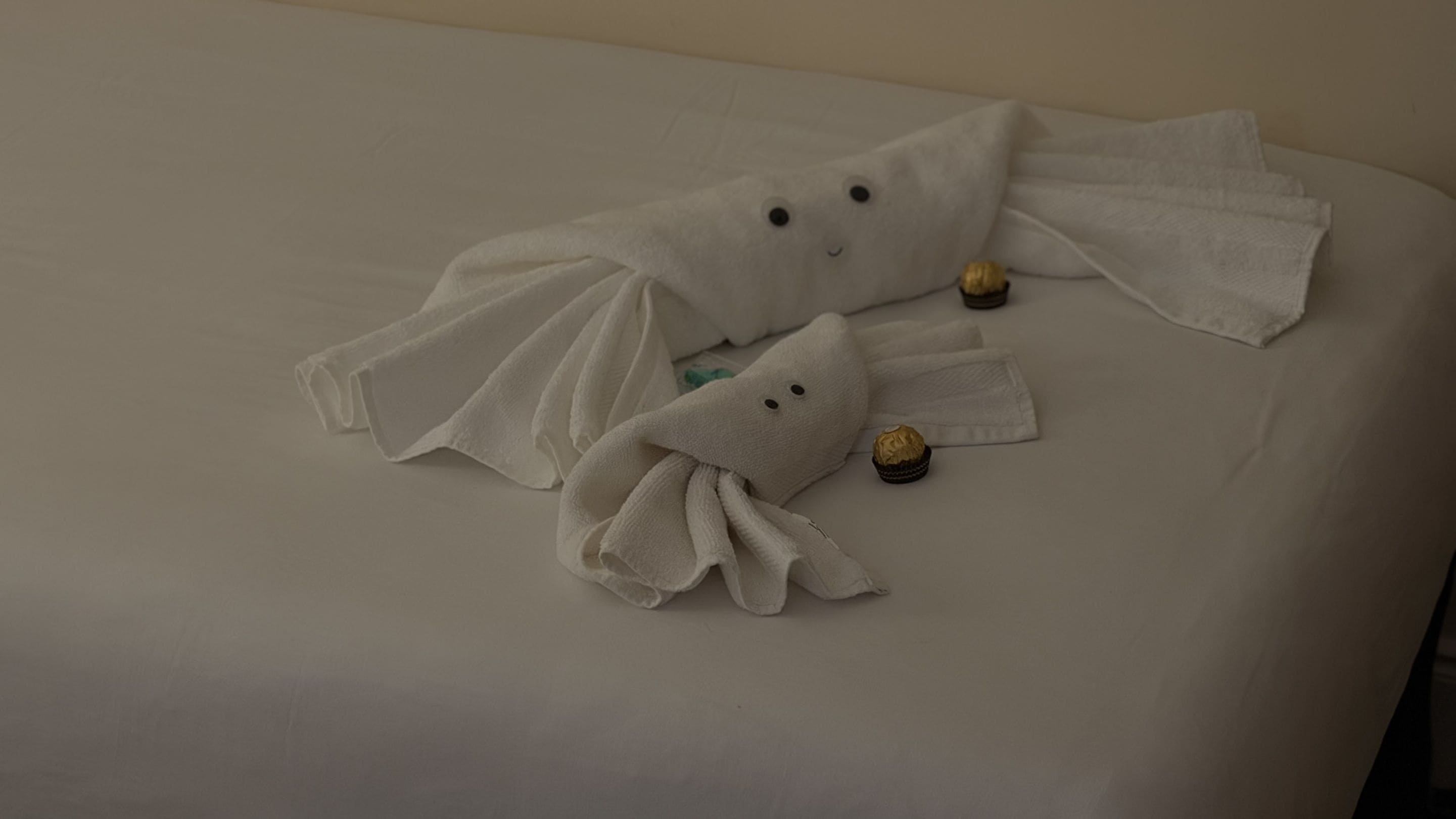 Una cama con dos toallas con forma de fantasma y un pequeño objeto envuelto.