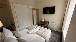 A hotel room with a bed, a bedside table with a kettle, a flat-screen TV, a radiator, and a mirror. - Waverley Guest House (Inverness)