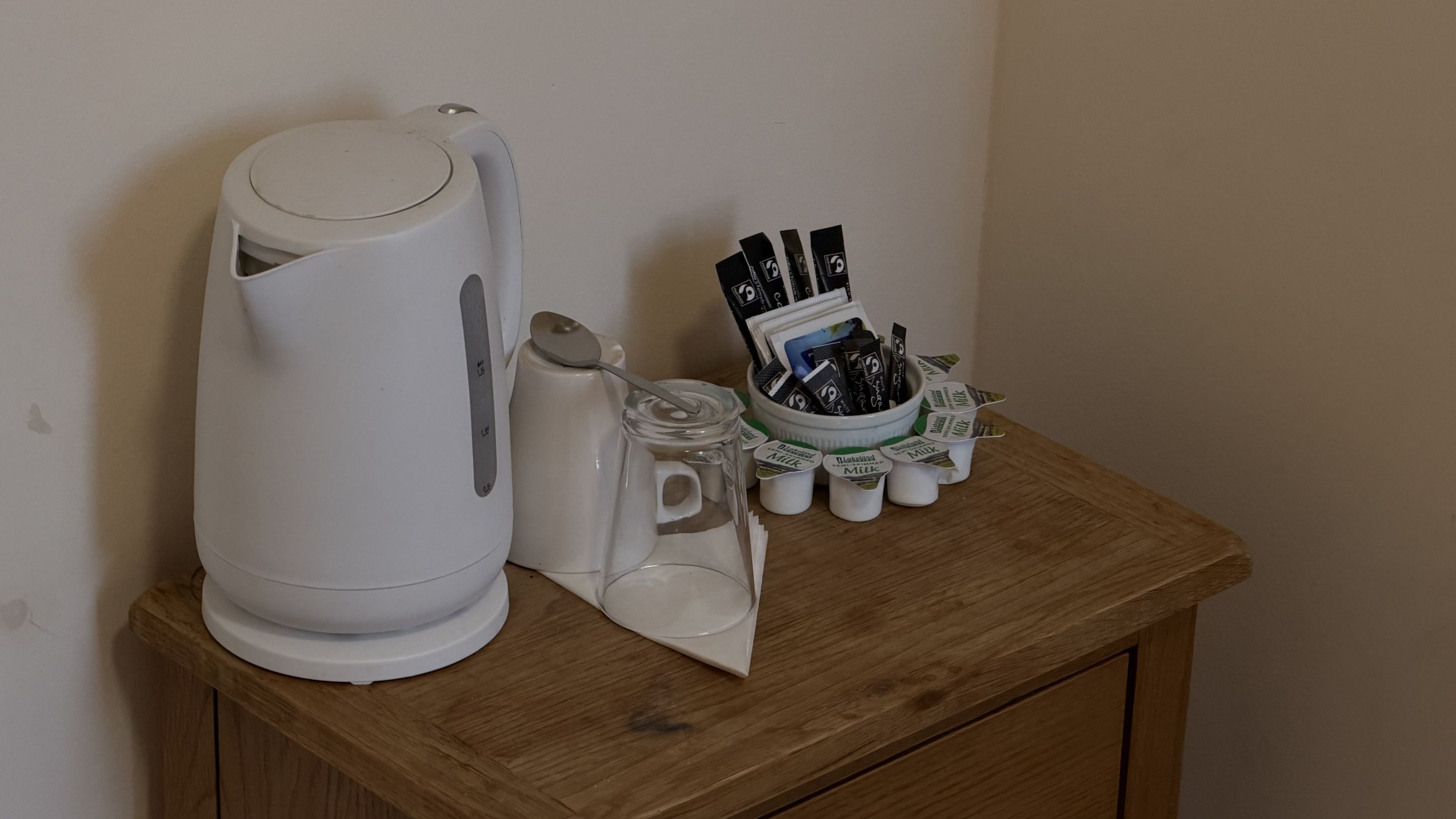 A kettle, a glass jar, and a milk carton holder on a wooden table.
