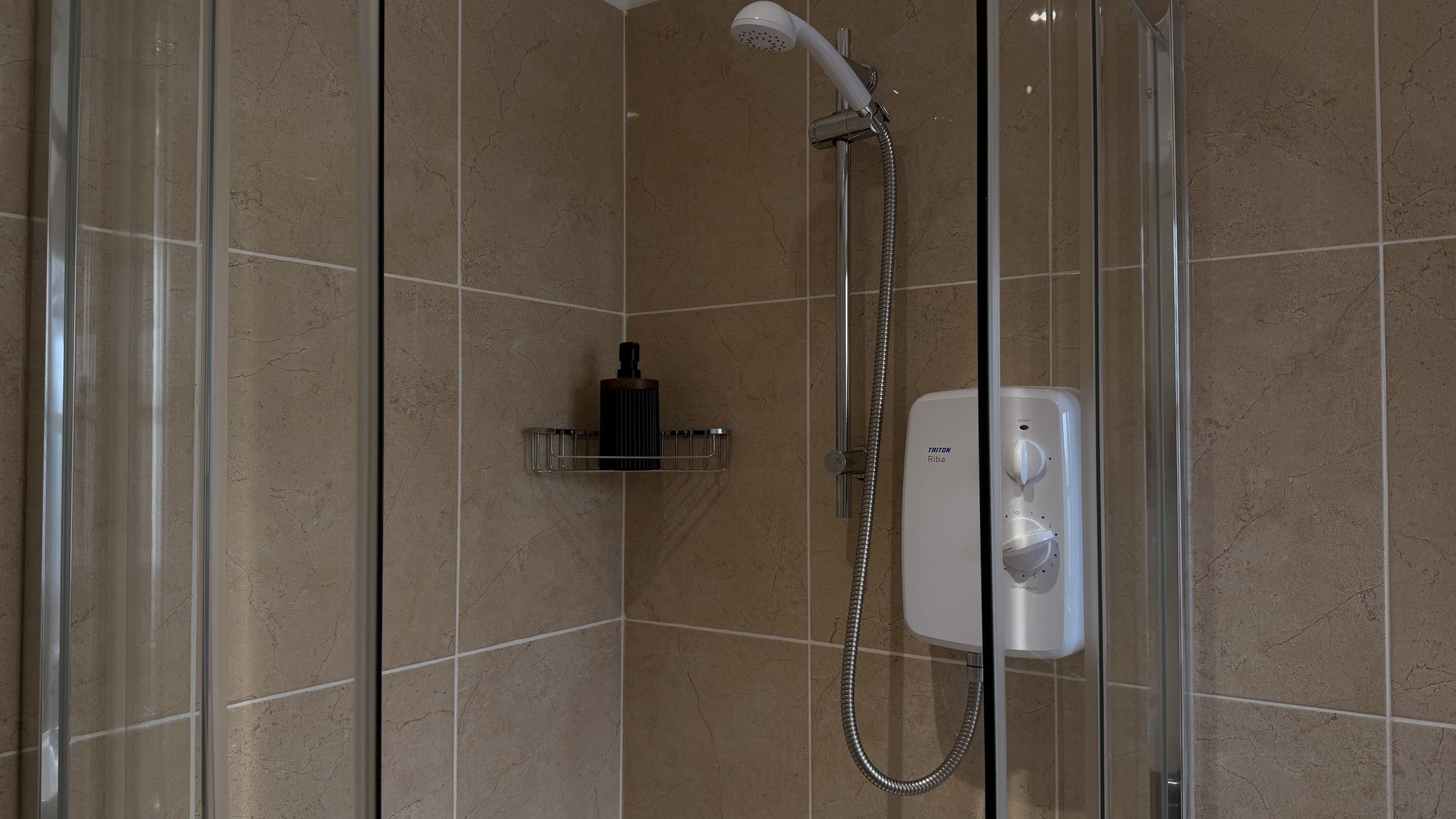 A glass-enclosed shower with a handheld showerhead and a wall-mounted control panel.