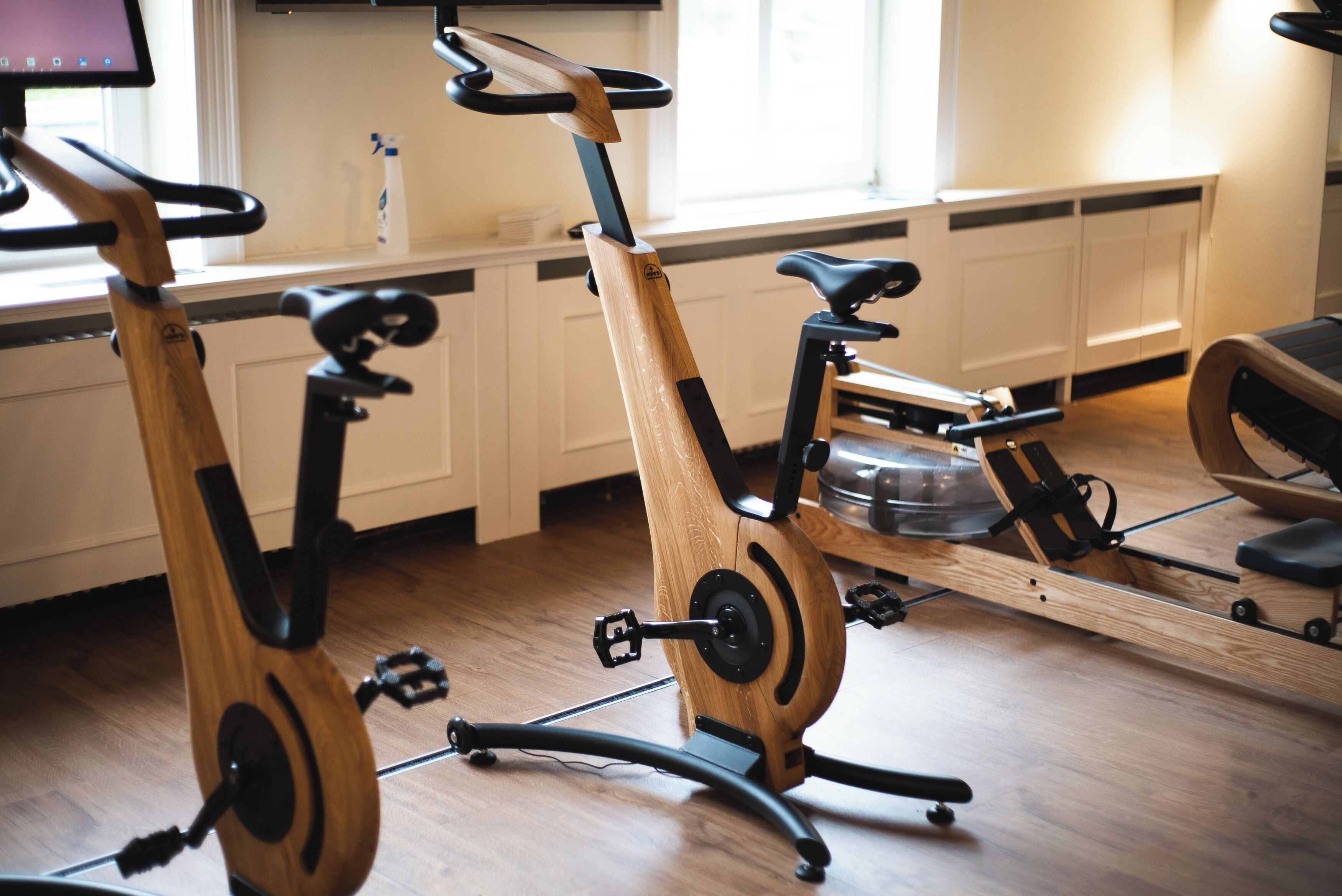 Two stationary bikes in a room with wooden flooring, white cabinets, and a window.