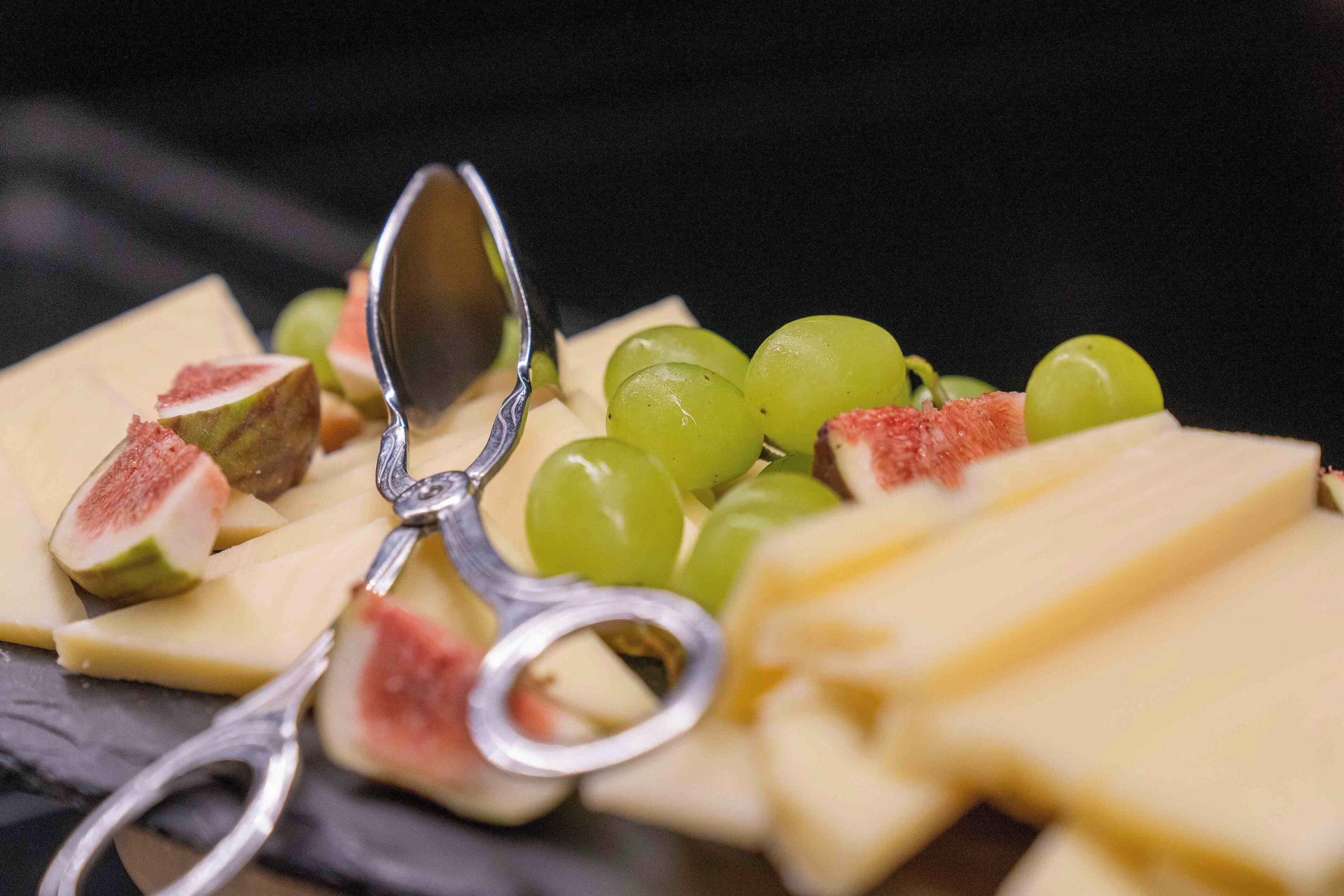 A variety of cheeses and fruits on a dark surface.