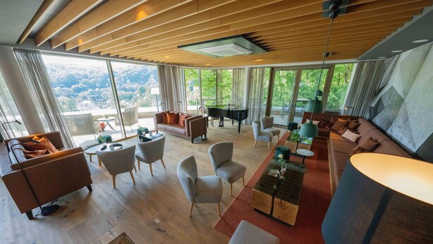 Amplia sala de estar con un piano, asientos cómodos y ventanas grandes que ofrecen vistas al exterior.