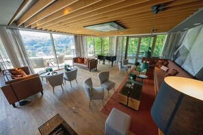 A spacious living area with a piano, comfortable seating, and large windows offering a view of the outdoors. - Hotel & Spa Suiten Freiwerk (Südharz)