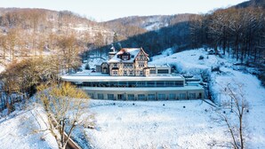 A large, historic building with a traditional architectural style, surrounded by a snowy landscape and a forested hillside. - Hotel & Spa Suiten Freiwerk (Südharz)