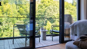 A balcony with a wooden floor, two chairs, a small table with a plant, and a view of a forested area. - Hotel & Spa Suiten Freiwerk (Südharz)