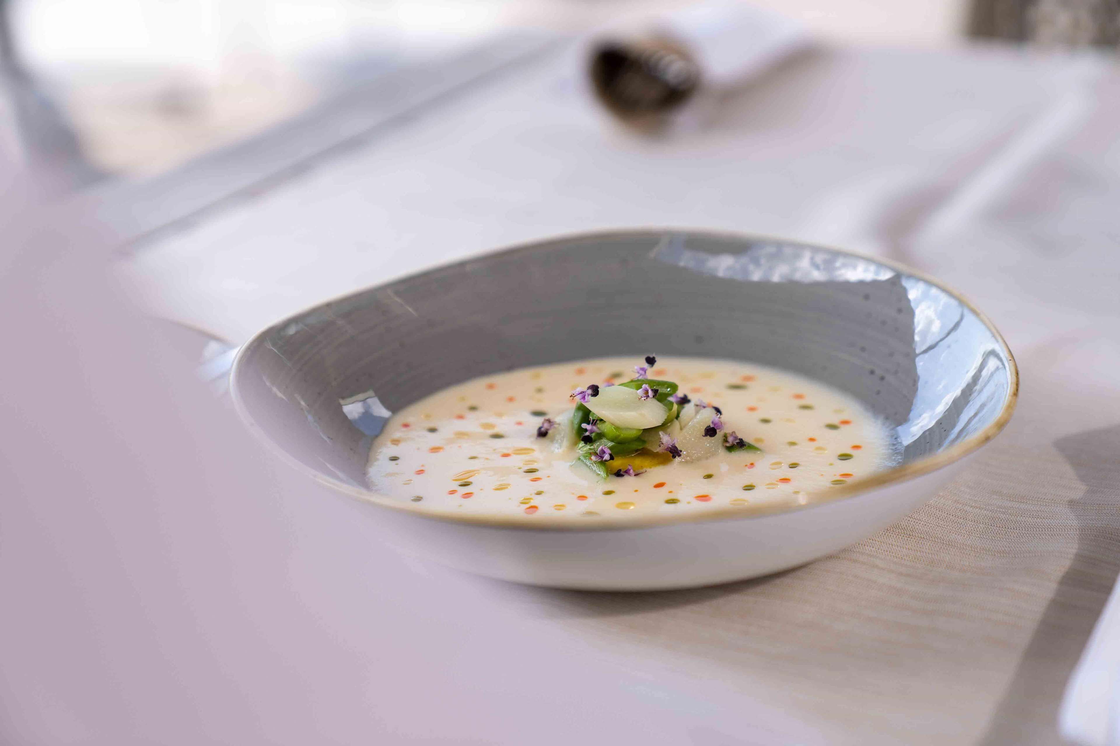 Una ciotola di zuppa con base cremosa e guarnita con erbe aromatiche e fiori commestibili.