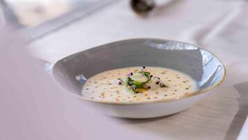 Una ciotola di zuppa con base cremosa e guarnita con erbe aromatiche e fiori commestibili.