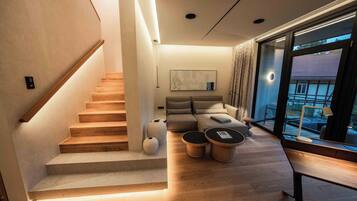 Un salón moderno con una escalera de madera, un conjunto de sofás y un amplio ventanal con vistas.