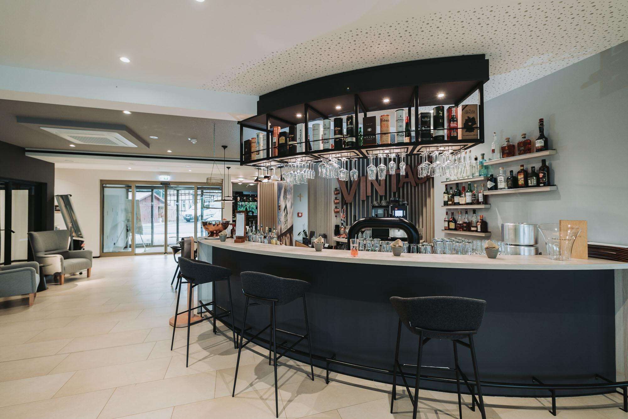 Eine moderne Bar mit einer gebogenen Theke, Barhocker und einer Auswahl an Flaschen und Gläsern.