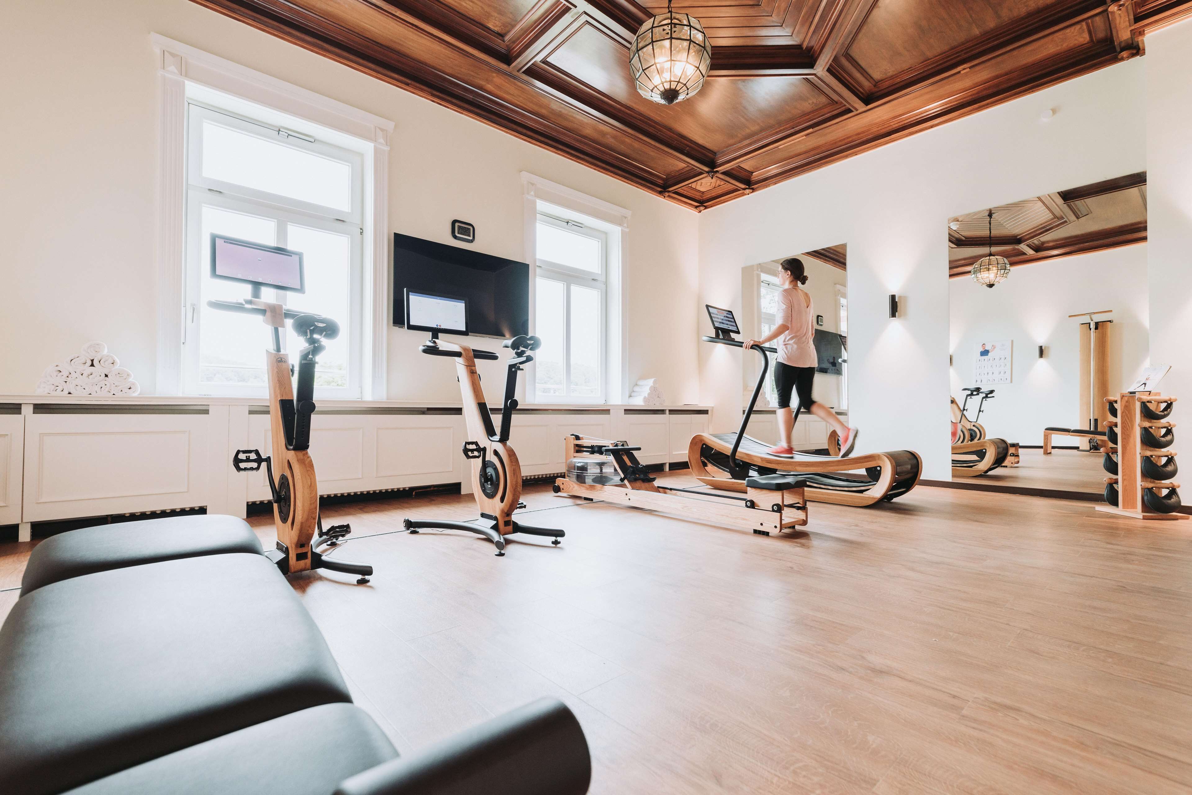Un gimnasio con equipo de ejercicio, ventanas amplias y detalles en techo de madera.
