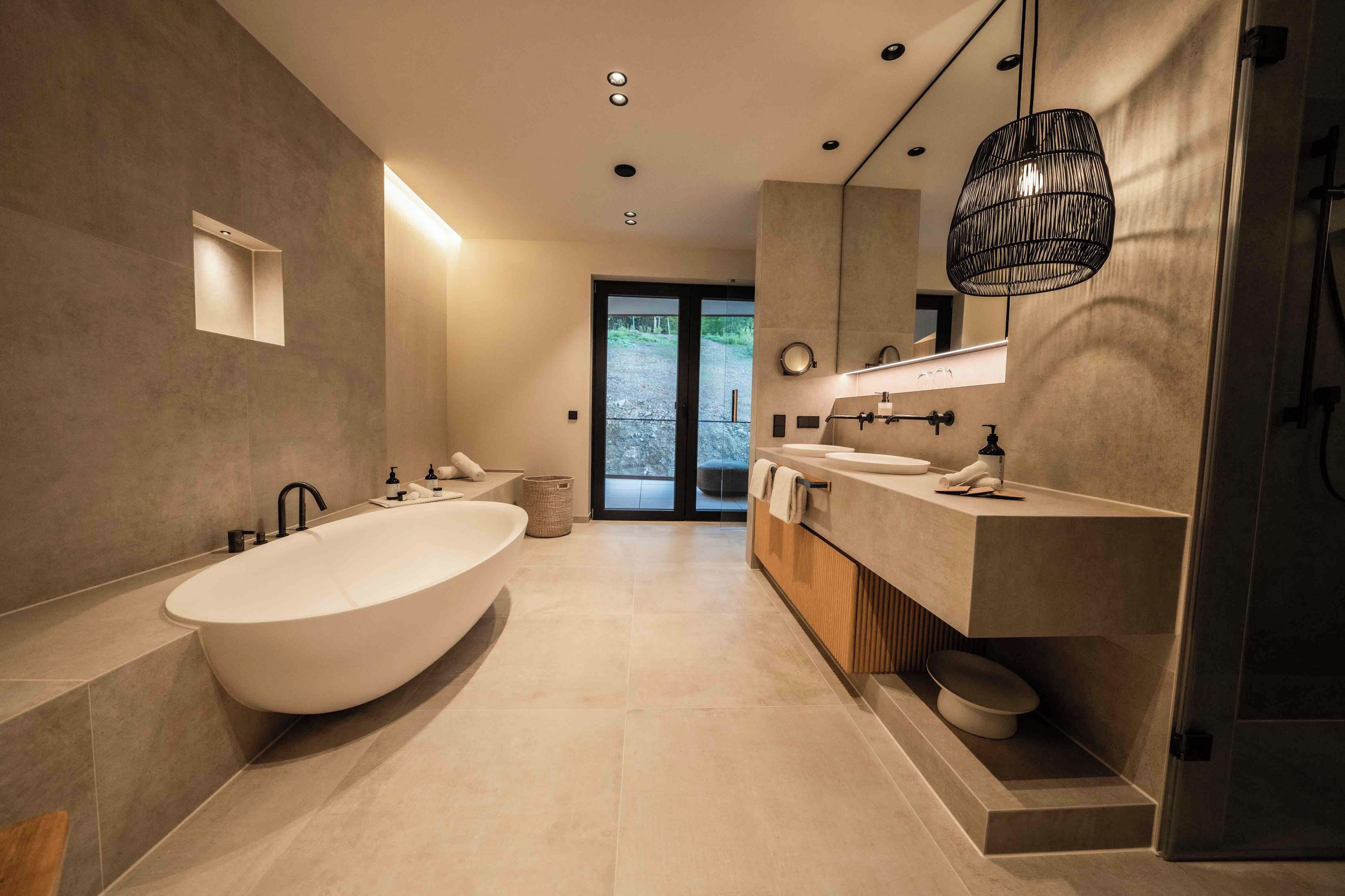 Ein modernes Badezimmer mit einer freistehenden Badewanne, einem großzügigen Waschtisch mit Spiegel und einer Pendelleuchte.