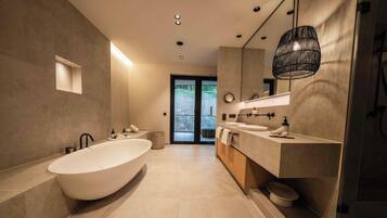 Un baño moderno con una bañera independiente, un tocador amplio con un espejo y una lámpara colgante.