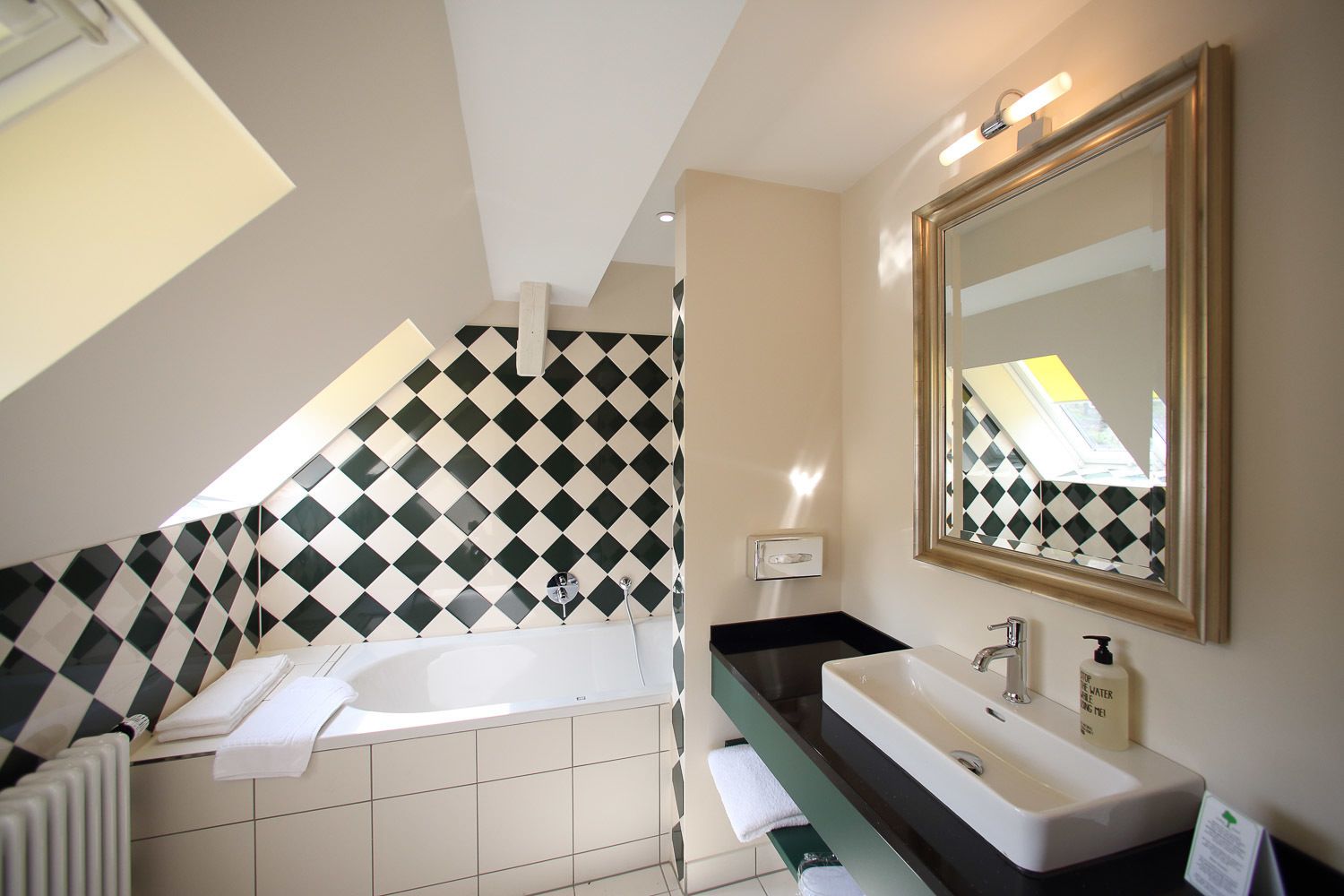 Een moderne badkamer met een vrijstaand bad, een grote spiegel en een zwart aanrecht met een wastafel.