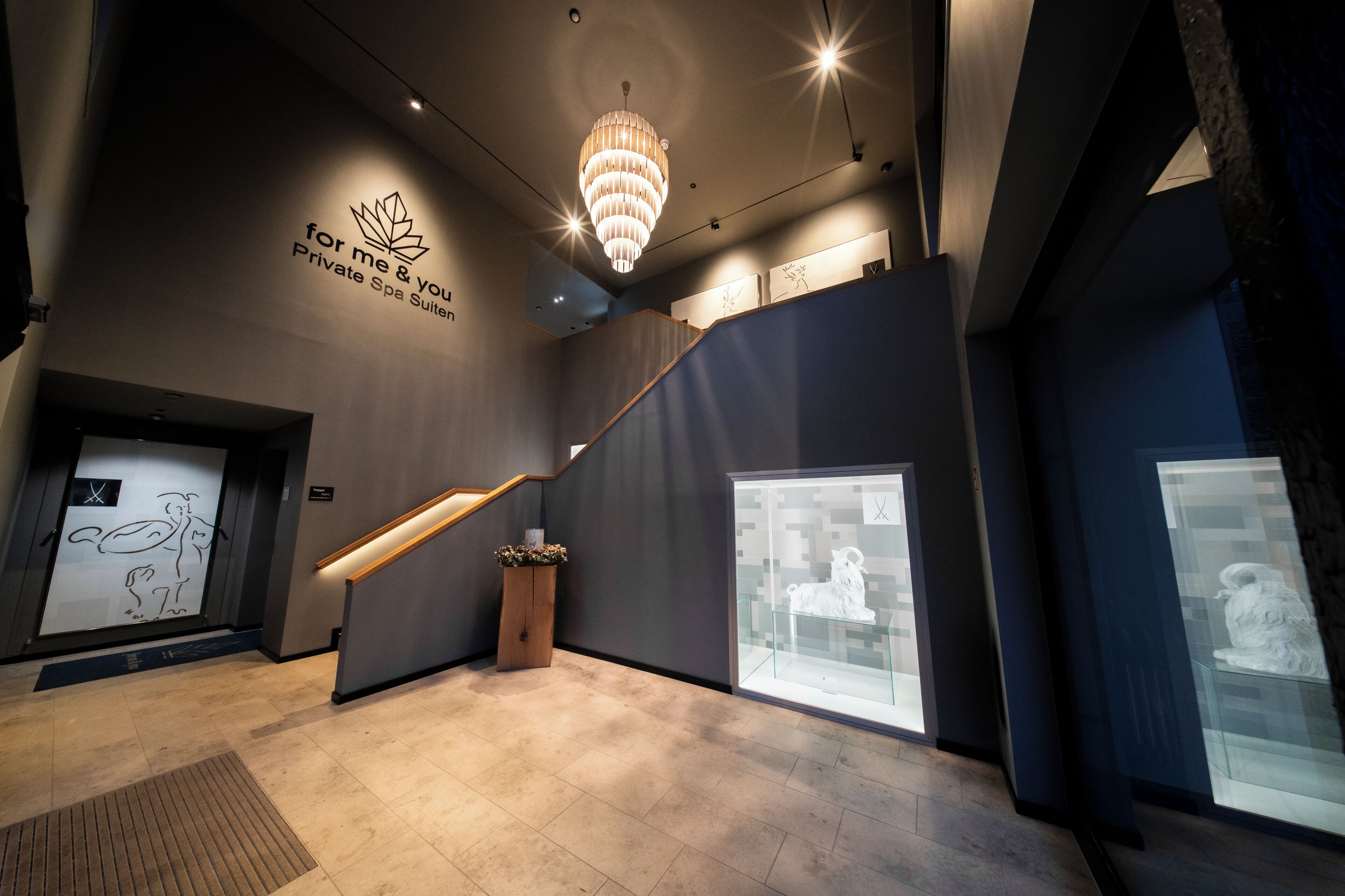 A modern interior with a staircase, a chandelier, and artwork on the walls.