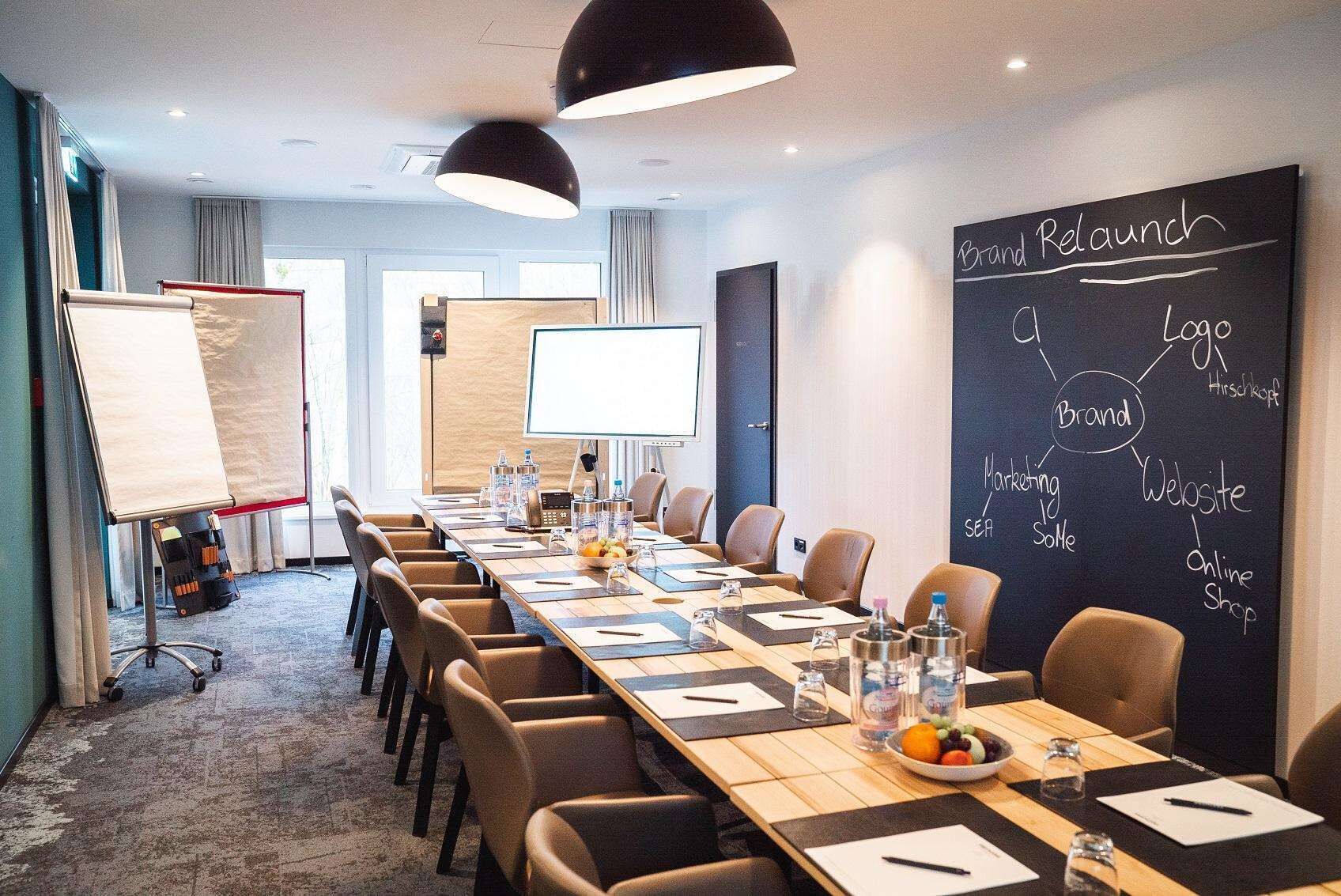 Ein Konferenzraum mit langem Tisch, Stühlen, einer Tafel und einer Schiefertafel mit Branding-Elementen.