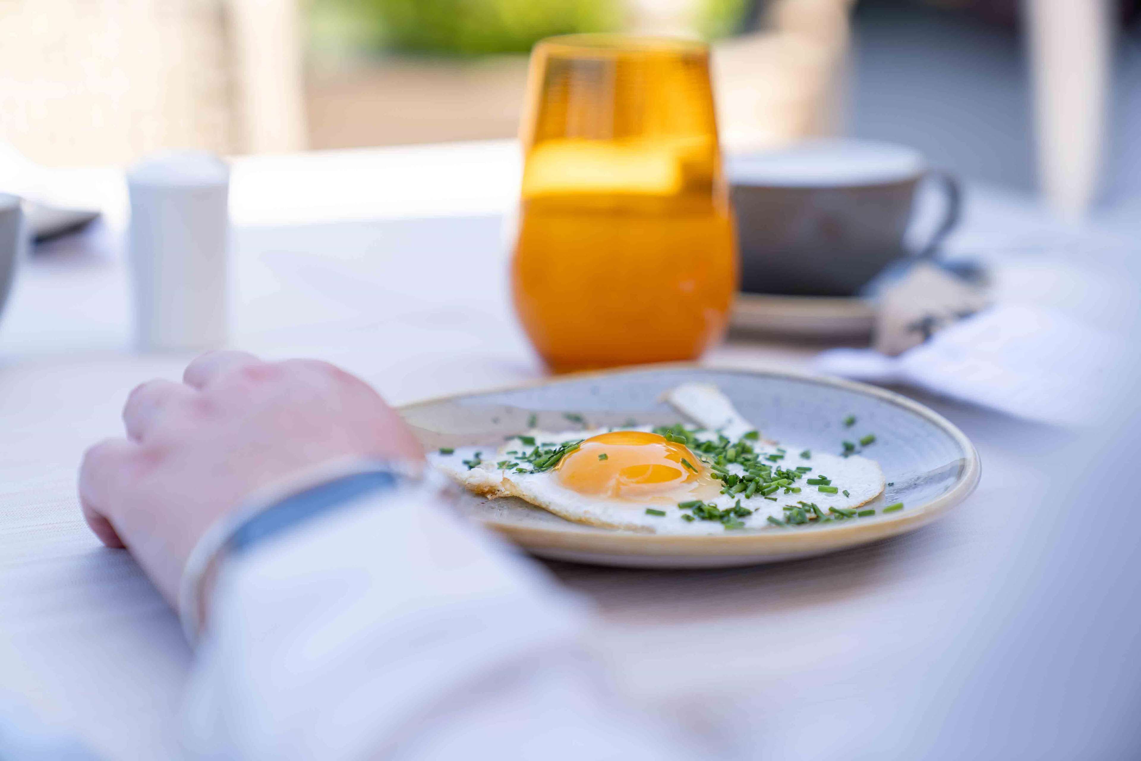 Un desayuno con un plato de huevos fritos adornados con cebollín, un vaso de jugo de naranja y una taza de café sobre una mesa.