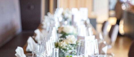 A long dining table with clear glassware, white napkins, and floral centerpieces.