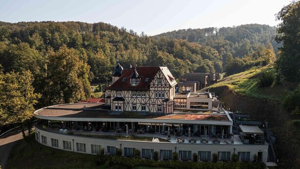 A modern building with a traditional half-timbered structure, surrounded by lush greenery and hills. - Hotel & Spa Suiten Freiwerk (Südharz)