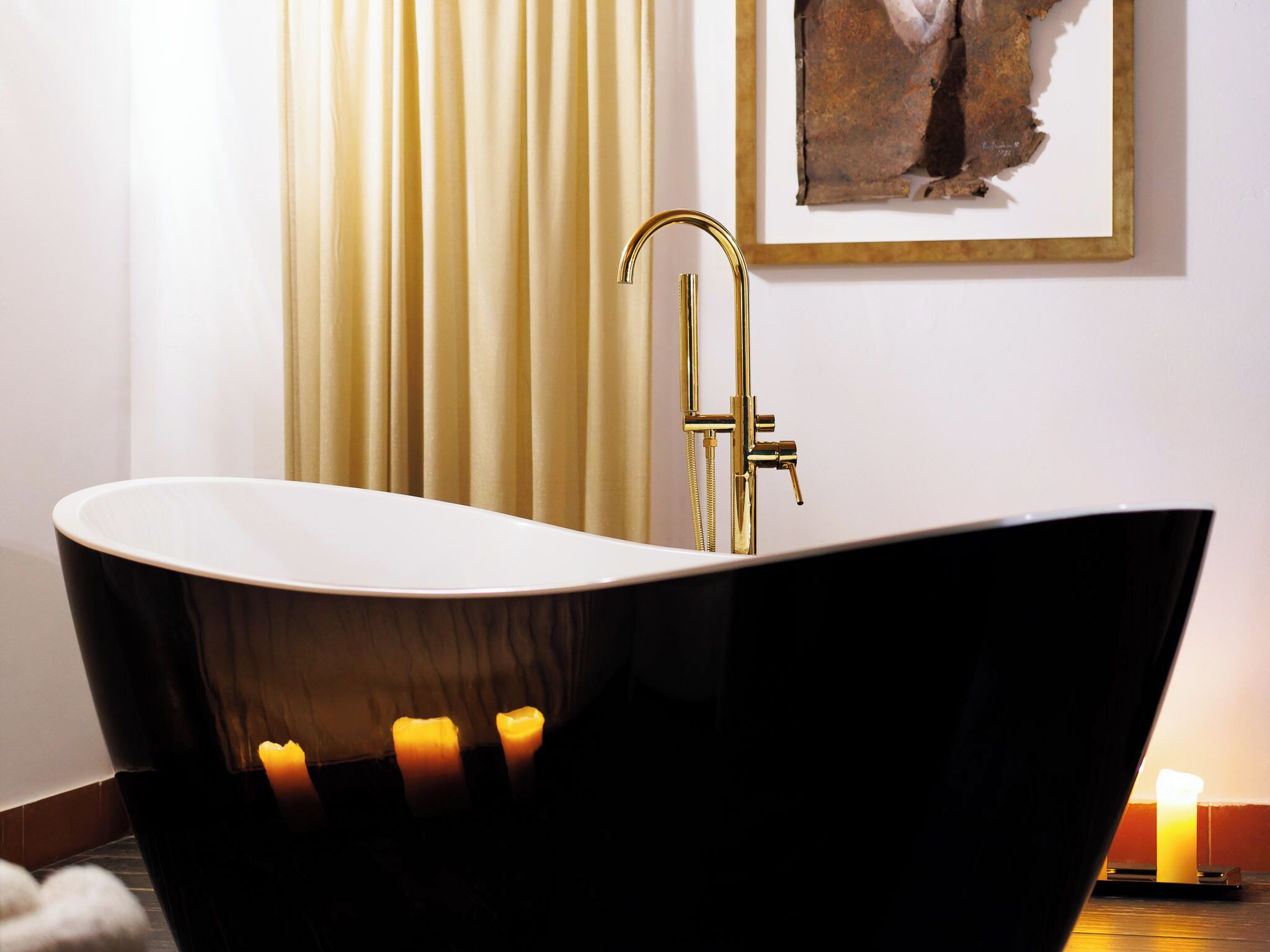 A modern bathroom with a freestanding bathtub, a gold faucet, and candles on the floor.