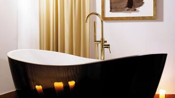 A modern bathroom with a freestanding bathtub, a gold faucet, and candles on the floor.