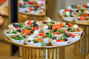 Una mesa de buffet con pequeñas fuentes de ensalada, que incluye tomates, aceitunas y vegetales verdes.