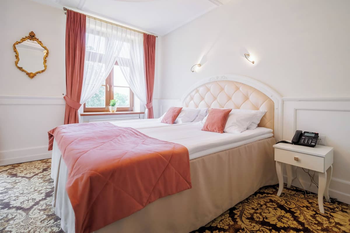 Une chambre d’hôtel avec un grand lit, une table de chevet avec un téléphone et une fenêtre avec des rideaux légers.