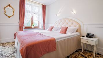 Habitación de hotel con una cama grande, una mesita de noche con teléfono y una ventana con cortinas traslúcidas.