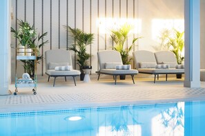 Zona de piscina con sillas de descanso, plantas en macetas y un carrito de toallas.