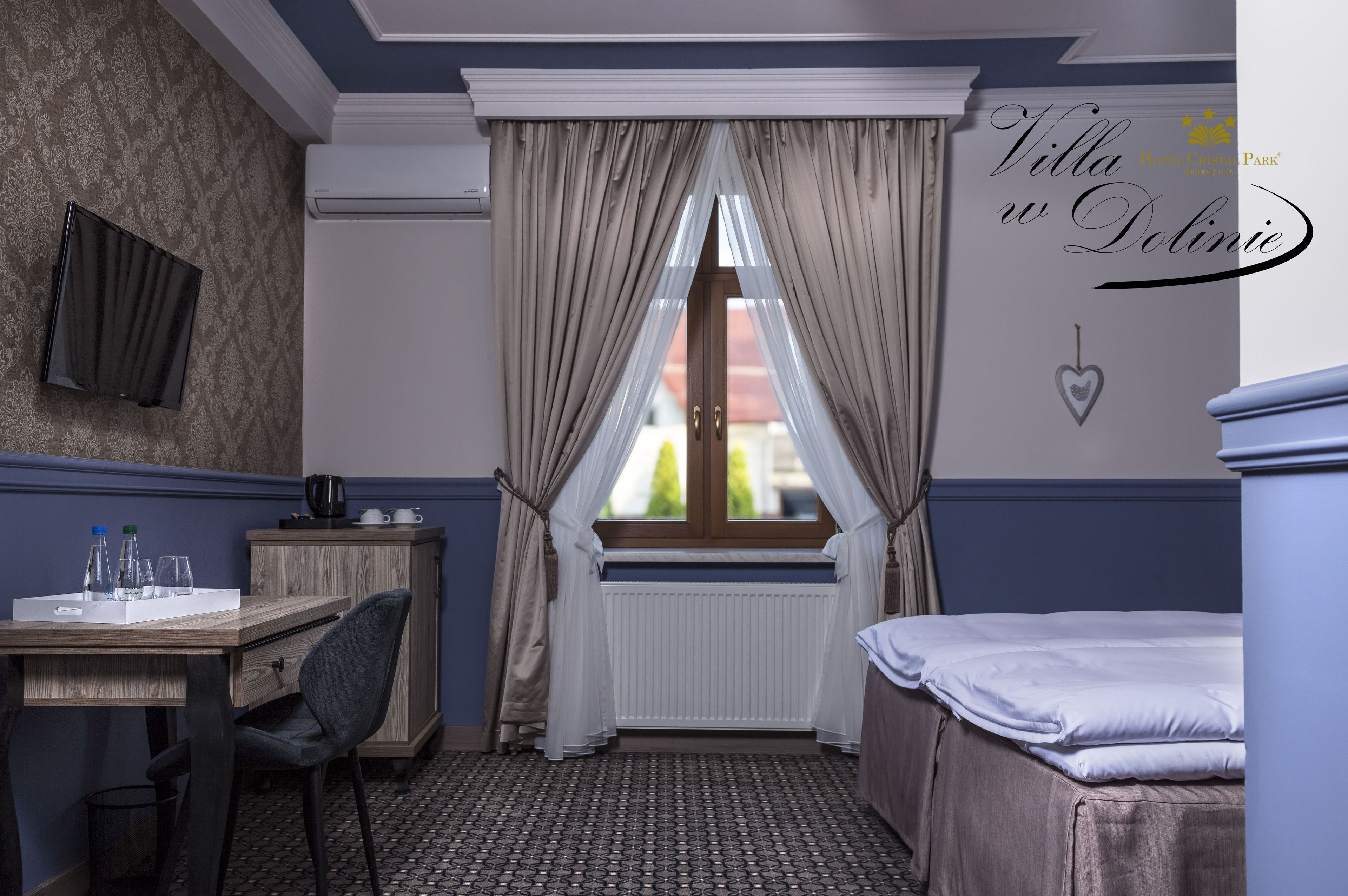 A hotel room with a wooden desk, a chair, a bed, and a window with curtains.